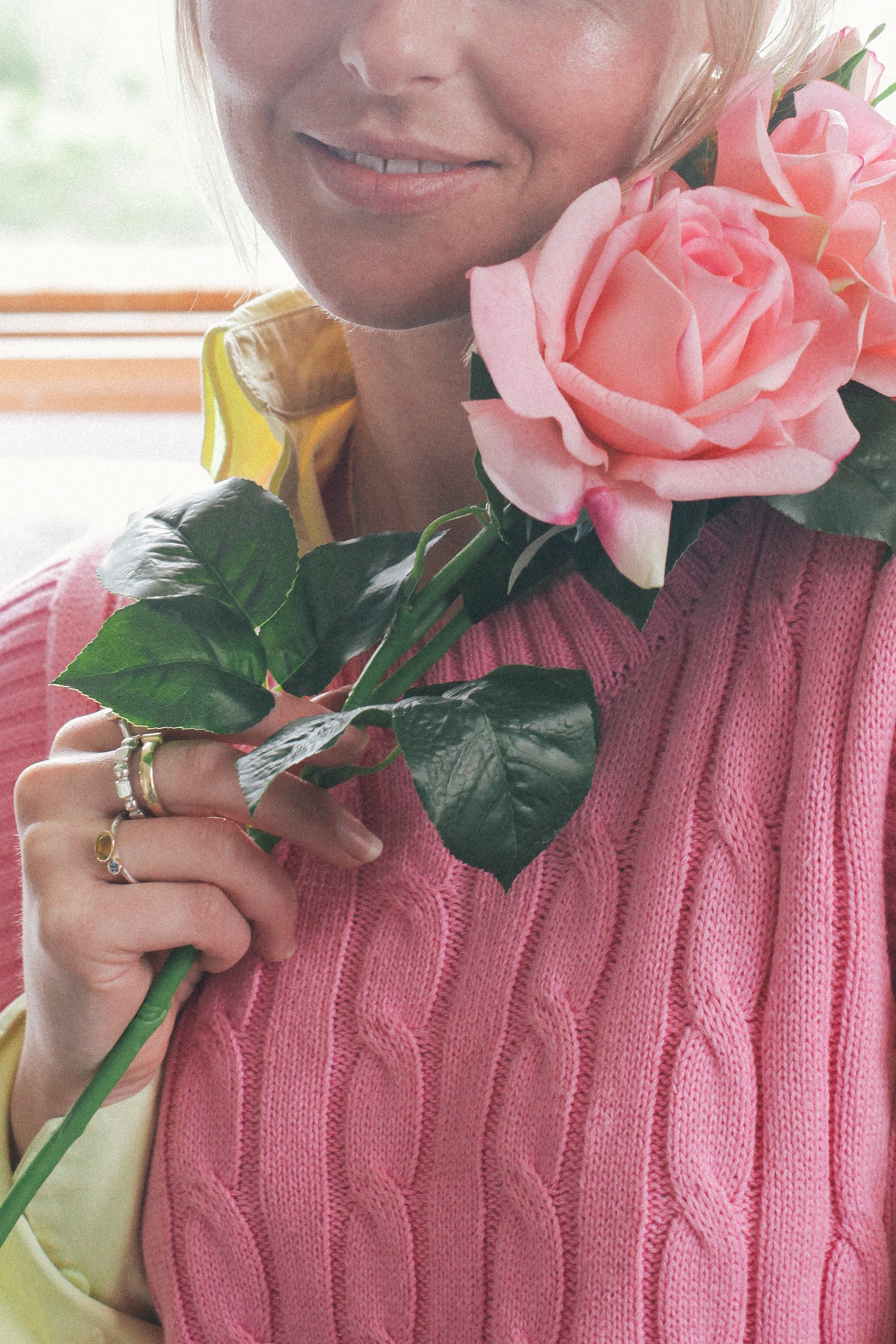 Person wearing a pink sweater holding pink roses faux flowers 